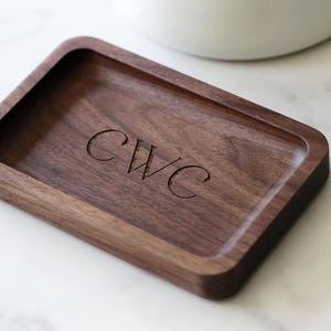 May include: A rectangular wooden tray with a dark brown finish. The tray has a raised edge and is engraved with the initials "CWC".