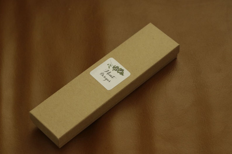 Puede incluir: Una caja de cart&oacute;n marr&oacute;n con una pegatina blanca que dice "Mint Designs" y un dise&ntilde;o de hoja verde.