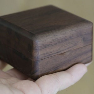 May include: A dark brown wooden box with a hinged lid. The box is made of a dark wood with a natural grain pattern.
