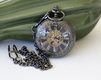 May include: A black pocket watch with a silver face and Roman numeral hour markers. The watch has a skeletonized movement and is attached to a black chain.