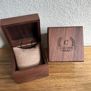 May include: A wooden box with a hinged lid and a velvet interior. The box is engraved with the letter "C" and the name "Caiden" in a wreath design.