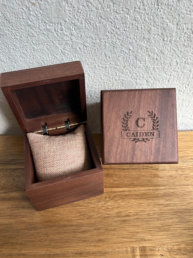 May include: A wooden box with a hinged lid and a velvet interior. The box is engraved with the letter "C" and the name "Caiden" in a wreath design.