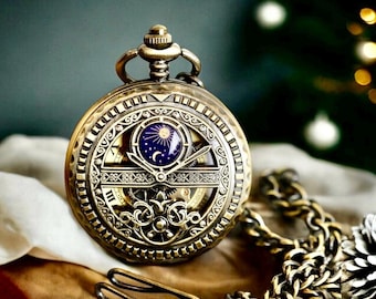 May include: A gold-toned pocket watch with a skeletonized design and a blue and gold celestial-themed face. The watch is attached to a gold chain.