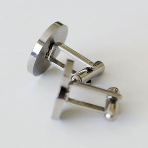 May include: A pair of silver cufflinks with a round, smooth surface. The cufflinks are connected by a silver bar.