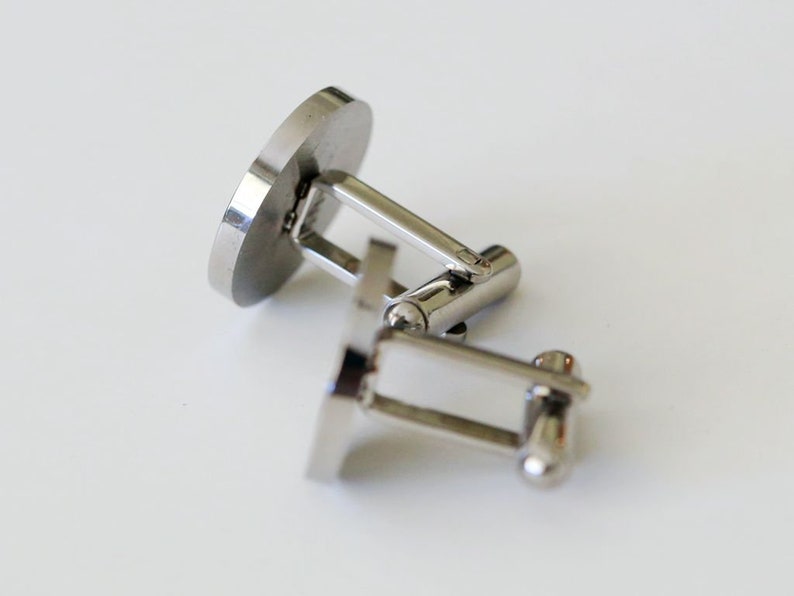 May include: A pair of silver cufflinks with a round, smooth surface. The cufflinks are connected by a silver bar.