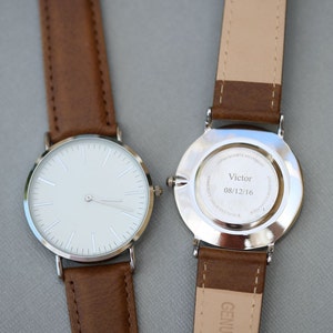 Puede incluir: Un reloj plateado con una esfera blanca y una correa de cuero marr&oacute;n. La parte posterior del reloj tiene una inscripci&oacute;n que dice "Victor 08/12/16".