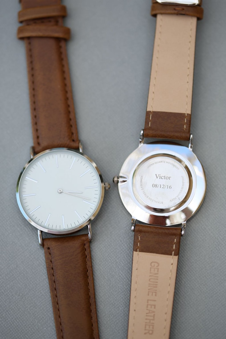 Puede incluir: Un reloj plateado con una esfera blanca y una correa de cuero marr&oacute;n. La parte posterior del reloj tiene una inscripci&oacute;n que dice "Victor 08/12/16".