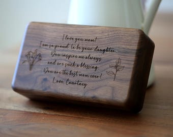 Può includere: Targa rettangolare in legno con bordi arrotondati, incisa con un messaggio sentito e illustrazioni floreali. Il testo recita "Ti amo mamma!" ed è firmato "Love, Courtney."
