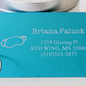 May include: A turquoise blue luggage tag with a white eye mask icon and the text "Briana Paluck", "1359 Gissing Pl", "RED WING, MN 55066", and "(510) 553-3877".