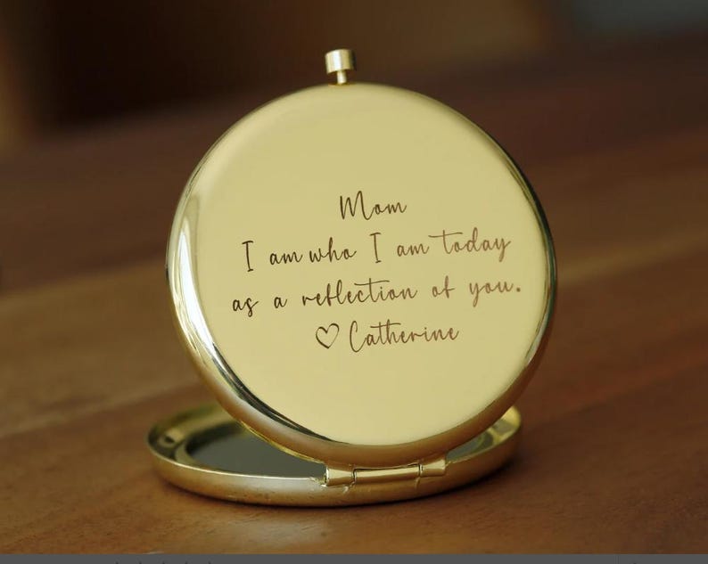 Op de afbeelding: Gouden compact spiegel met een gegraveerd bericht: "Mam, ik ben wie ik vandaag ben, omdat ik een weerspiegeling van jou ben. Catherine"