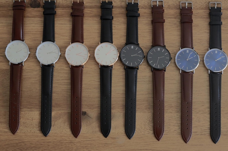 May include: Ten wristwatches with different colored faces and leather bands. The watches have silver, black, white, and blue faces. The bands are brown, black, and dark brown.