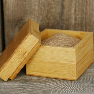 Puede incluir: Una caja de madera natural con tapa, la caja est&aacute; abierta y tiene un forro de tela de arpillera en el interior.