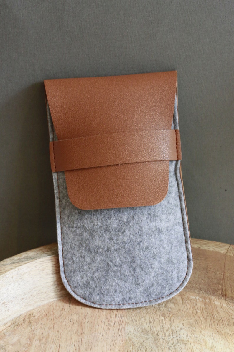 Puede incluir: Una bolsa de cuero marr&oacute;n y fieltro gris con cierre de solapa. La bolsa tiene una correa de cuero marr&oacute;n en la parte delantera.
