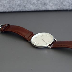 May include: A silver watch with a white face and brown leather band.
