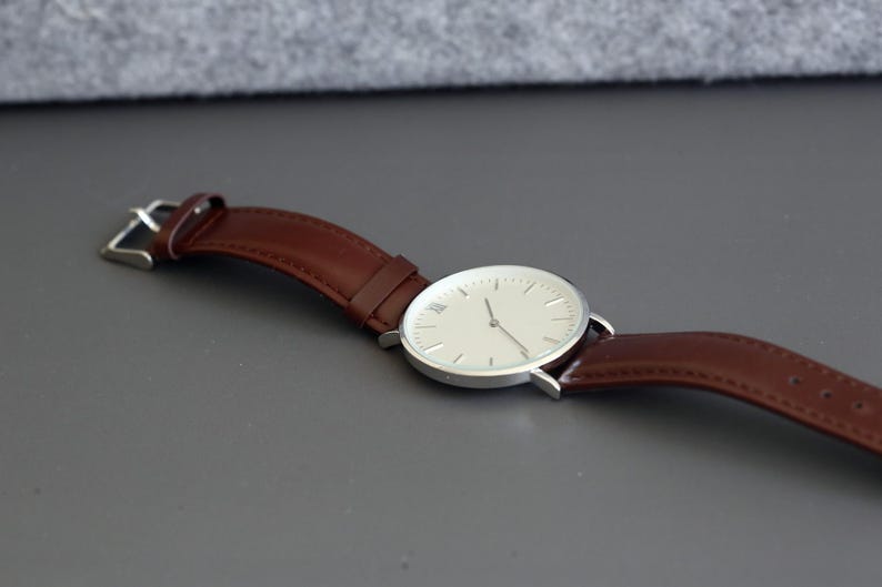 May include: A silver watch with a white face and brown leather band.