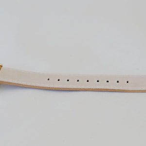May include: A gold-tone watch with a white leather band. The band has multiple holes for adjusting the fit.
