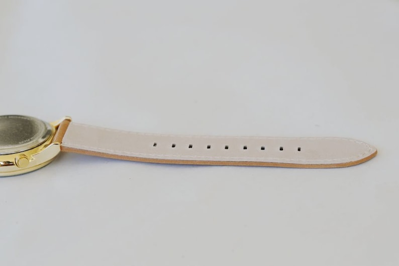 May include: A gold-tone watch with a white leather band. The band has multiple holes for adjusting the fit.