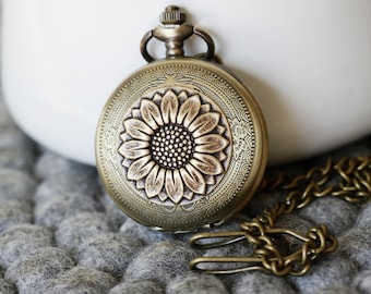 May include: A gold-toned pocket watch with a sunflower design on the face and a chain attached.