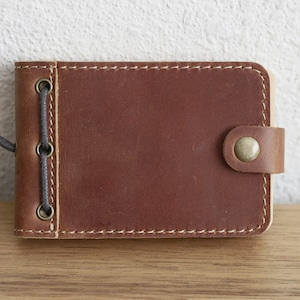 May include: A brown leather notebook with a flap closure and a gray cord tie. The notebook has three metal eyelets on the left side and a metal button on the flap.