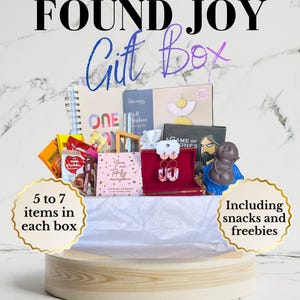 Könnte beinhalten: Eine Geschenkbox mit einem Spiralnotizbuch, einem Set zur Herstellung von Wandanhängern, einem Kartenspiel, einer kleinen rosa Schachtel mit dem Text You are Totally awesome, einer roten Schmuckschatulle mit Ohrringen und einer blauen Figur.
