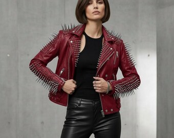 May include: A red leather jacket with silver spikes on the shoulders and sleeves. The jacket has a classic biker style with a zipper closure and a notched collar. The model is wearing a black top and black leather pants.