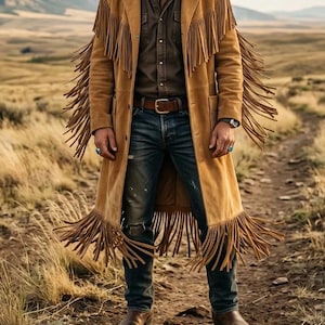 May include: A tan suede long coat featuring long fringe detailing along the shoulders, sleeves, and hem. The coat is worn over a dark brown button-up shirt, a brown leather belt with a silver buckle, blue denim jeans, and brown leather boots.