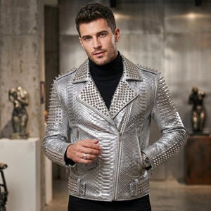 Op de afbeelding: Een metallic zilveren motorjas met een slangenleerachtige textuur, voorzien van een brede revers, een asymmetrische ritssluiting aan de voorzijde en zilveren metalen studs op de schouders, revers en mouwen, gedragen over een zwart coltruitje.