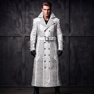 Könnte beinhalten: Ein langer weißer Trenchcoat mit doppelreihiger Knopfleiste, passendem Taillengürtel mit Schnalle sowie zahlreichen schwarzen Metallnieten und Stacheln an den Schultern, Ärmeln, Revers und über die gesamte Länge des Mantels verteilt.