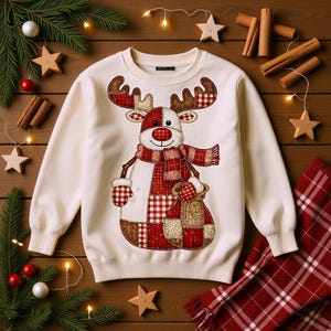 Peut inclure: Pull de Noël crème avec un motif de renne aux accents écossais rouges et blancs. Le renne a un nez rouge, une écharpe assortie et un sac. Le pull est entouré de décorations festives, dont des bâtons de cannelle et des ornements en forme d'étoile.