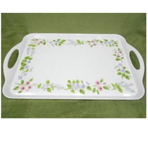May include: A rectangular white serving tray with integrated side handles, featuring a delicate floral border pattern of small pink and light blue flowers with green leaves arranged along the edges of the flat surface of the tray.