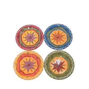 May include: A set of four round ceramic plates featuring hand-painted designs. Each plate displays a central star-like floral motif surrounded by concentric rings of contrasting colours including red, green, blue, and orange with white dots.