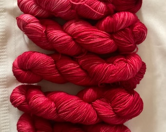 May include: Five skeins of vibrant red yarn are arranged on a white, textured surface. The yarn appears soft and fluffy, with subtle variations in color, creating a visually appealing texture. Ideal for knitting or crochet projects.