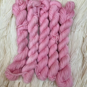 May include: Close-up of several skeins of pink yarn arranged on a background of white yarn. The pink yarn is tightly wound, showing a twisted texture. The white yarn is loosely arranged, creating a contrasting backdrop for the pink yarn.