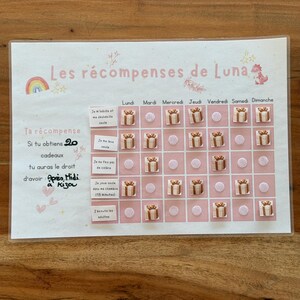 Peut inclure: Un tableau de récompenses rose et blanc avec le texte "Les récompenses de Luna". Le tableau comporte un arc-en-ciel, des étoiles et un motif de licorne. Il comprend des espaces pour les tâches quotidiennes et les récompenses.
