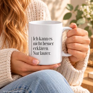 Könnte beinhalten: Eine weiße Keramiktasse mit schwarzem Aufdruck, der lautet: Ich kann es nicht besser erklären. Nur lauter. Die Tasse hat einen glatten, zylindrischen Körper mit einem geschwungenen Henkel auf der rechten Seite für heiße oder kalte Getränke.