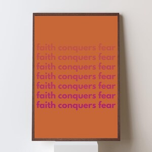 May include: Framed art print with an orange background and the phrase "faith conquers fear" repeated in a pinkish-purple font. The frame is a dark brown color. The artwork is displayed on a white wall.