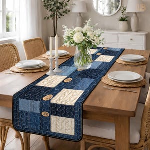 May include: A blue denim-style table runner with a quilted design. The runner features squares of varying blue shades and cream-colored knit-look fabric, accented with wooden buttons. The runner is approximately 183 cm long.