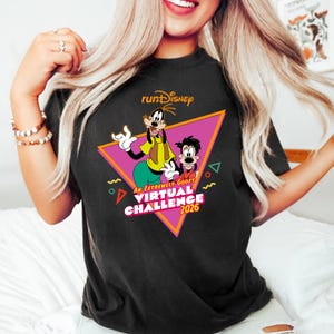 Puede incluir: Camiseta negra con un diseño de RunDisney que presenta a Goofy y Max. El gráfico incluye un triángulo rosa con el texto "An Extremely Goofy Virtual Challenge 2026". La camiseta tiene cuello redondo y mangas cortas.