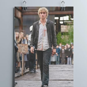 May include: A poster showing a man in a dark jacket, white shirt, and dark trousers walking on a wooden walkway. The poster is held by two black binder clips. A sign that says "GIRLS 14-16" is visible.