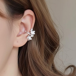 Op de afbeelding: Zilverkleurige oor manchet met een bloemenontwerp. De manchet wikkelt zich om het oor met delicate, driedimensionale bloemdetails. De sieraden worden op het bovenste oor gedragen en voegen een vleugje elegantie toe. Het ontwerp is ingewikkeld en gedetailleerd.
