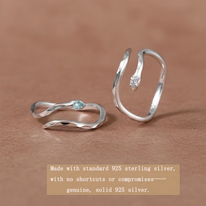 May include: Two silver snake rings. One ring has a light blue gemstone, the other a clear gemstone. The rings are made of 925 sterling silver. The image text reads: Made with standard 925 sterling silver, with no shortcuts or compromises—genuine, solid 925 silver.