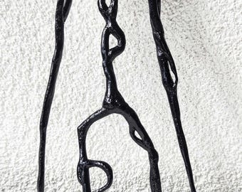 May include: A black, glossy, three-dimensional sculpture featuring a rounded head, elongated arms reaching downward, and a slender, interconnected torso structure. The figure has a smooth, reflective surface and stands on thin, pointed appendages.