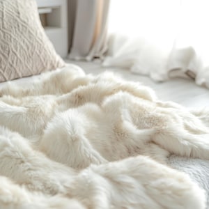 May include: A plush, off-white faux fur throw blanket with a thick, shaggy texture draped over a bed. The blanket features long, soft synthetic fibres in a creamy white tone, creating a dense and layered appearance across the surface.