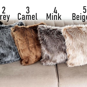 Pu&ograve; includere: Sei cuscini in finta pelliccia in vari colori: nero, grigio, cammello, visone, beige e bianco. I cuscini sono disposti su un divano chiaro. Ogni cuscino &egrave; etichettato con un numero e il nome del colore.