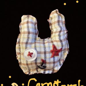 May include: A handmade fabric item in a U-shape, with a cream, brown, and yellow plaid pattern. It has a white button with a red cross, a red star, and a small anchor. The word "Cornstarch" is written in yellow.