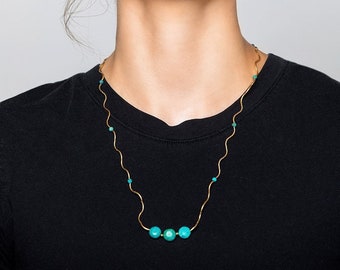 May include: A woman wearing a black shirt with a gold chain necklace with turquoise beads.