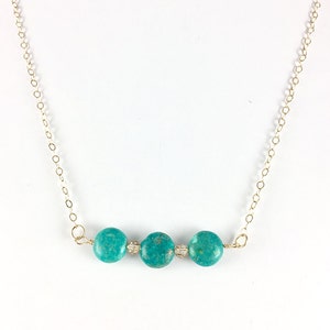 Puede incluir: Un collar de turquesa con tres piedras redondas en una cadena de oro.