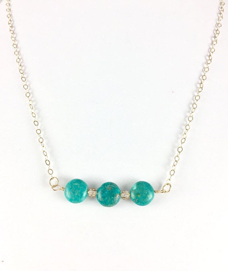 Puede incluir: Un collar de turquesa con tres piedras redondas en una cadena de oro.