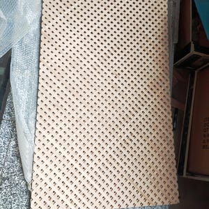 a rectangular piece of wood with a lattice pattern, sitting on a surface with a textured background.