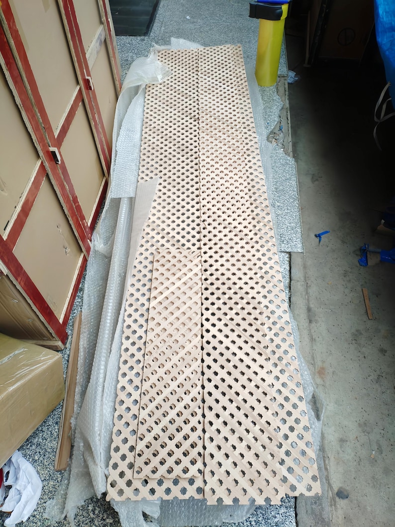 a long, perforated wooden plank lying on the ground, surrounded by cardboard boxes and other materials, suggesting it is being used for storage or construction purposes.